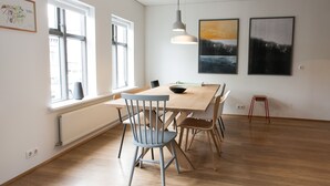 A dining area with a wooden table, chairs, and pendant lighting. - Mengi Apartments (Reykjavik)