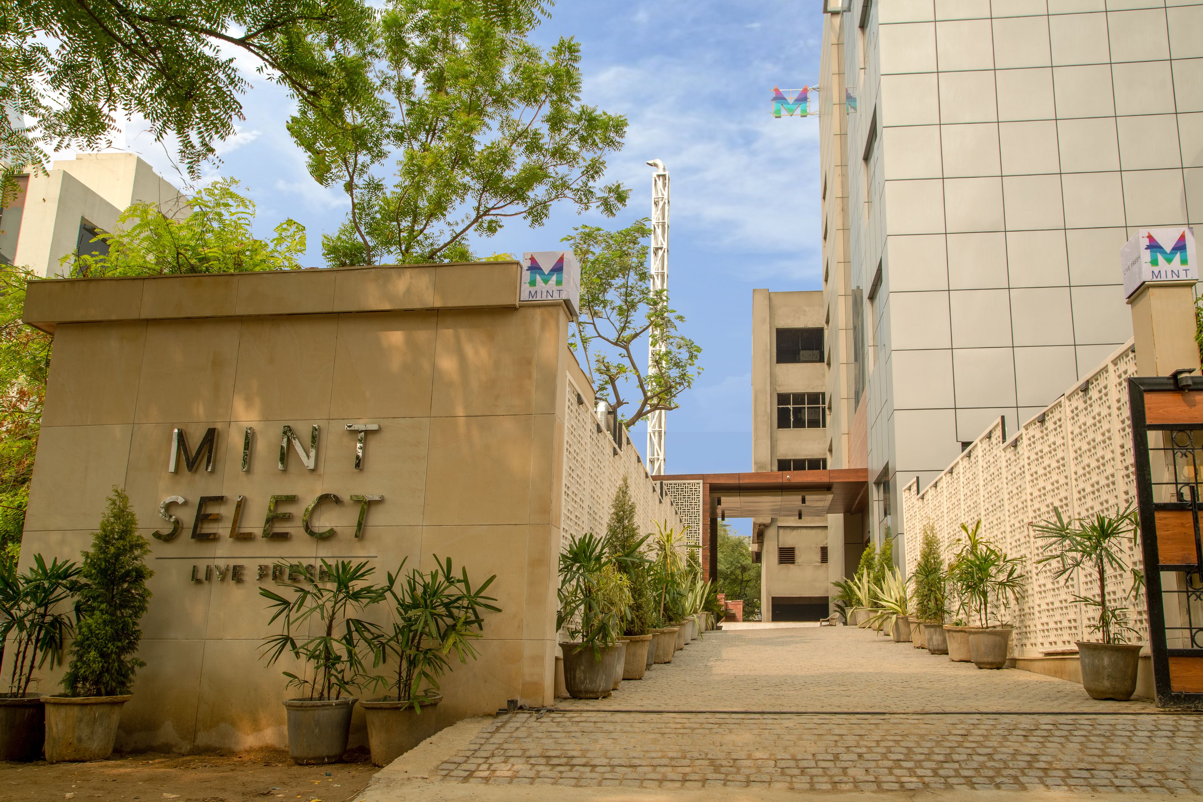 A building entrance with the sign "MINT SELECT LIVE FOOD" and potted plants lining the pathway.