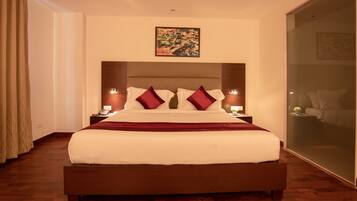 A large bed with a wooden frame, white bedding, and red pillows. There are two bedside tables with lamps. A painting is on the wall above the bed.