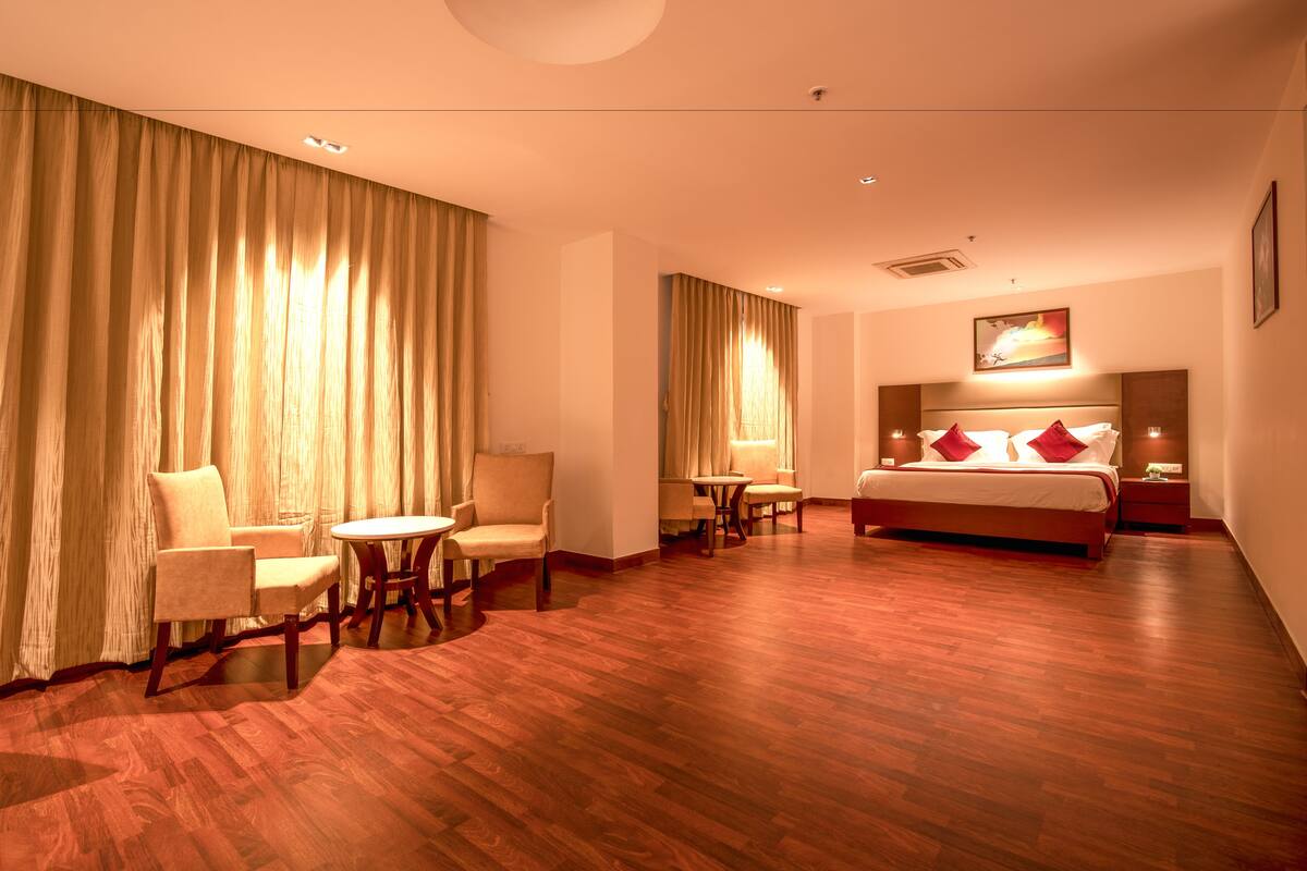 A hotel room with a large bed, two armchairs, a small table, and a large window with curtains.
