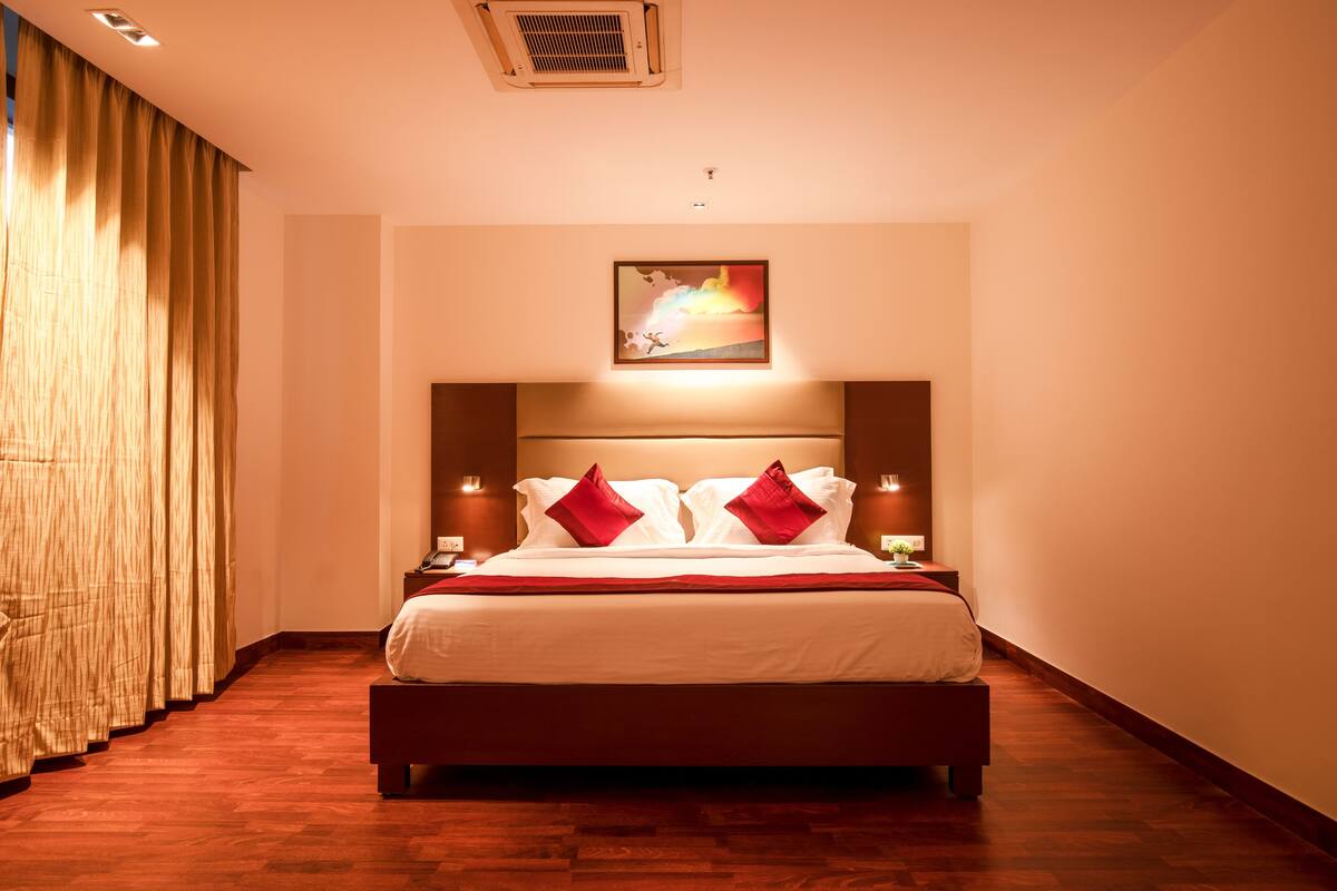 A neatly arranged hotel room with a large bed, a headboard with a painting, and two bedside lamps.