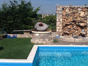 Une piscine avec un mur en pierre et une structure circulaire en pierre agrémentée d’un arrangement floral.