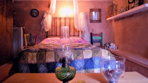 A cozy room with a bed, a table with a vase and a glass, and a shelf with decorative items. - Petrospito Pool Apt ''Katoi'', Faros Avlida (Chalcis)