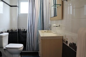 Een badkamer met toilet, wastafel, douchegordijn en spiegel.