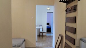 A narrow hallway with a bed on the left, a wooden chair in the center, and a desk with a chair in the background. - Shiny Modern Apartment • 1' to Metro Station (Athens)