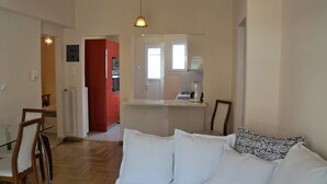 A living room with a sofa, a dining table with chairs, a kitchen area with a counter and appliances, and a red cabinet. - Shiny Modern Apartment • 1' to Metro Station (Athens)
