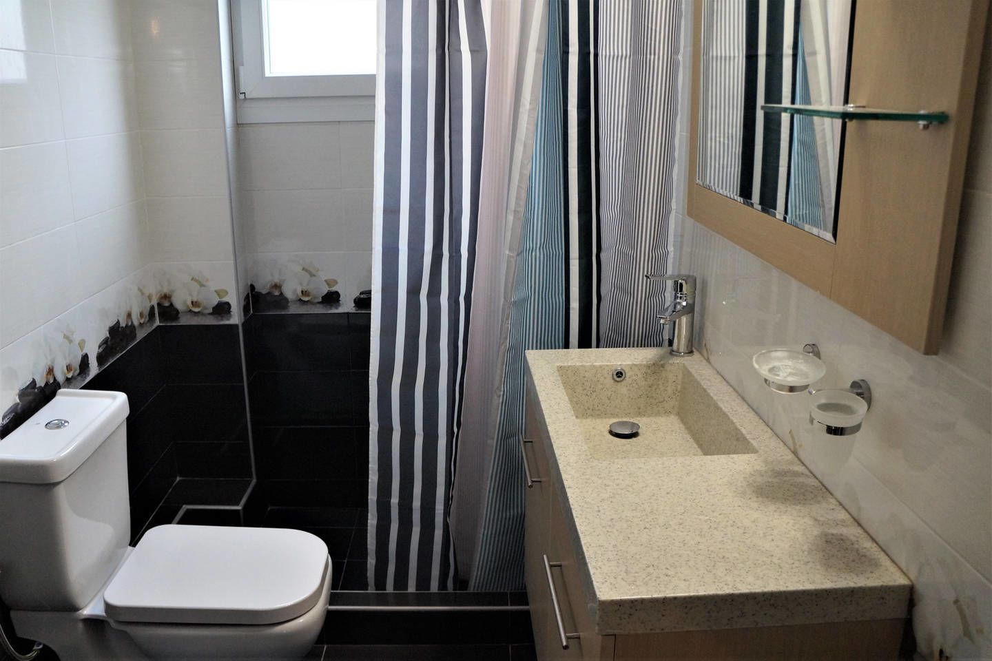Ein Badezimmer mit einer weißen Toilette, einem beige gefärbten Waschbecken mit zwei Wasserhähnen und einer Duschkabine mit gestreiften Vorhängen.