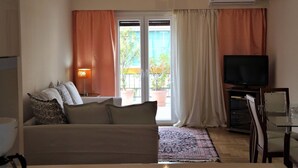 A living room with a sofa, a TV, and a balcony with potted plants. - Shiny Modern Apartment • 1' to Metro Station (Athens)