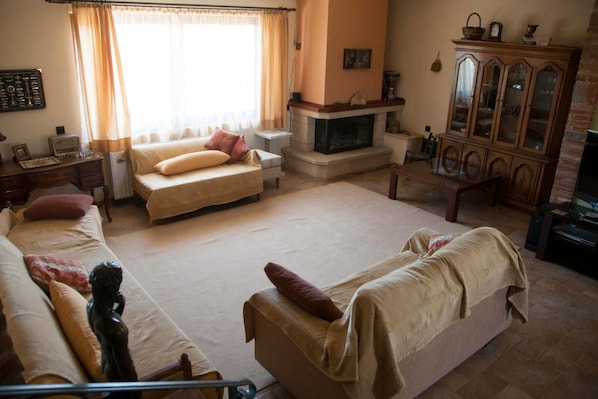 A spacious living room with a fireplace, a sofa set, a dining table, and a cabinet.