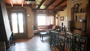 A living room with a sofa, a coffee table, and a railing. There is a door leading to another room and a window with curtains.