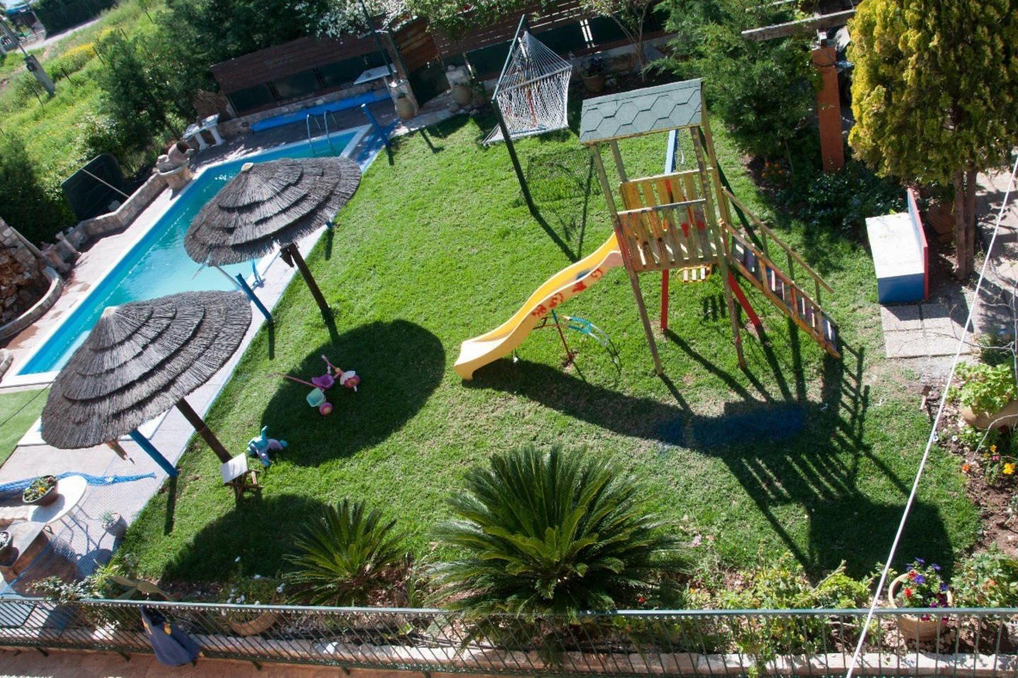 A backyard with a swimming pool, a slide, and a fenced area with a play structure.