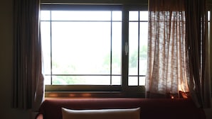 A room with a bed, a window with curtains, and a view of greenery outside.