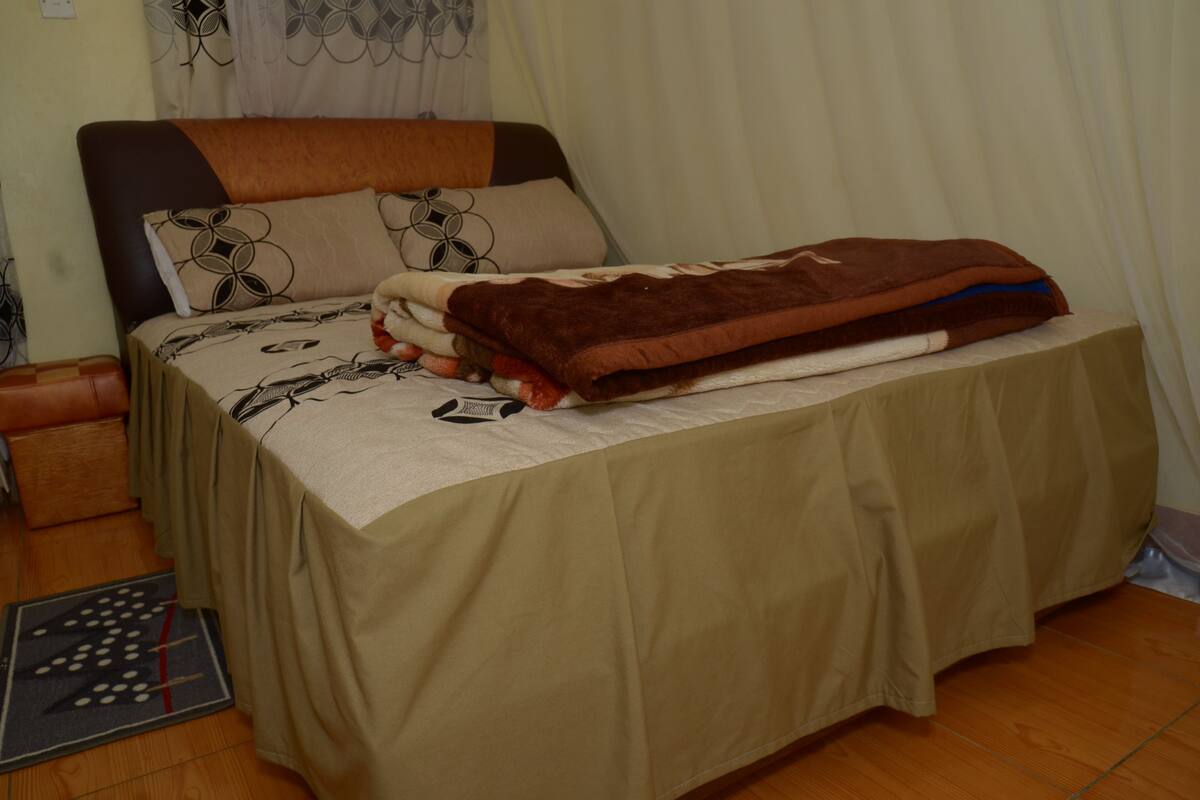 A neatly made bed with a patterned bedspread, a brown blanket, and a pillow with a geometric design.