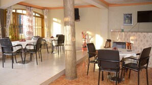 Un comedor con mesas y sillas, un pilar grande y un televisor en la pared.