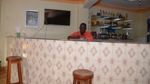 Zona de bar con pared de azulejos, un televisor montado en la pared y estantes llenos de botellas.