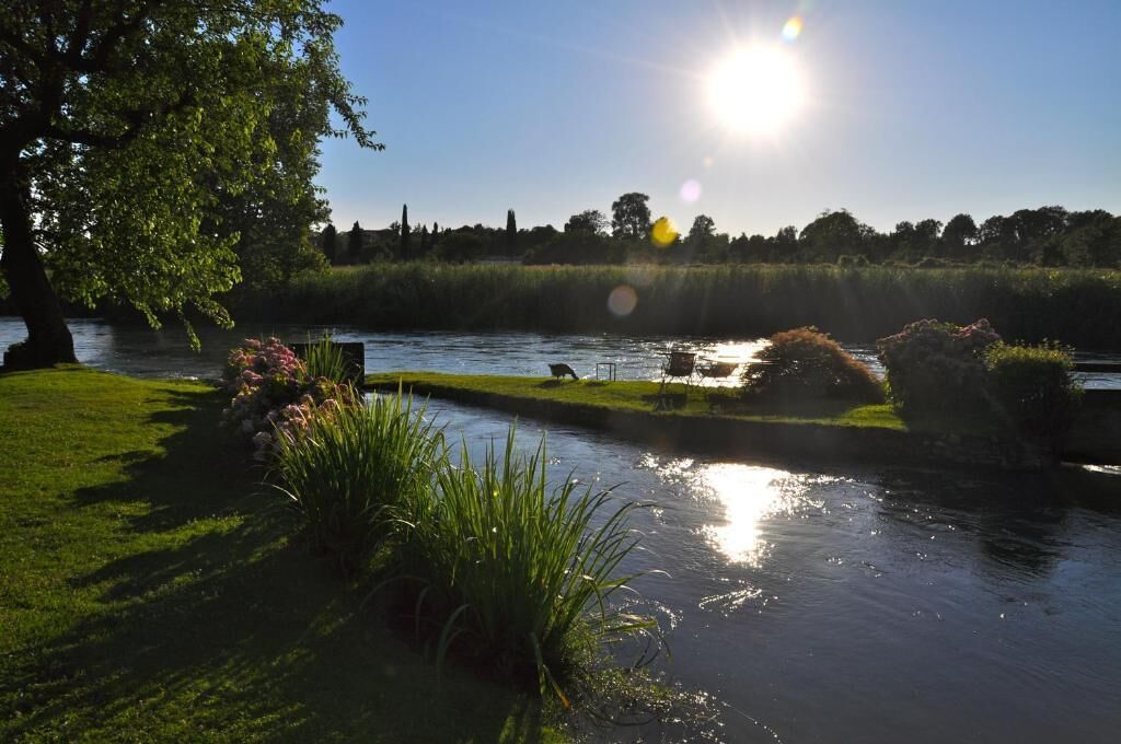 A serene riverside landscape with a clear sky, a sunlit water body, and lush greenery.