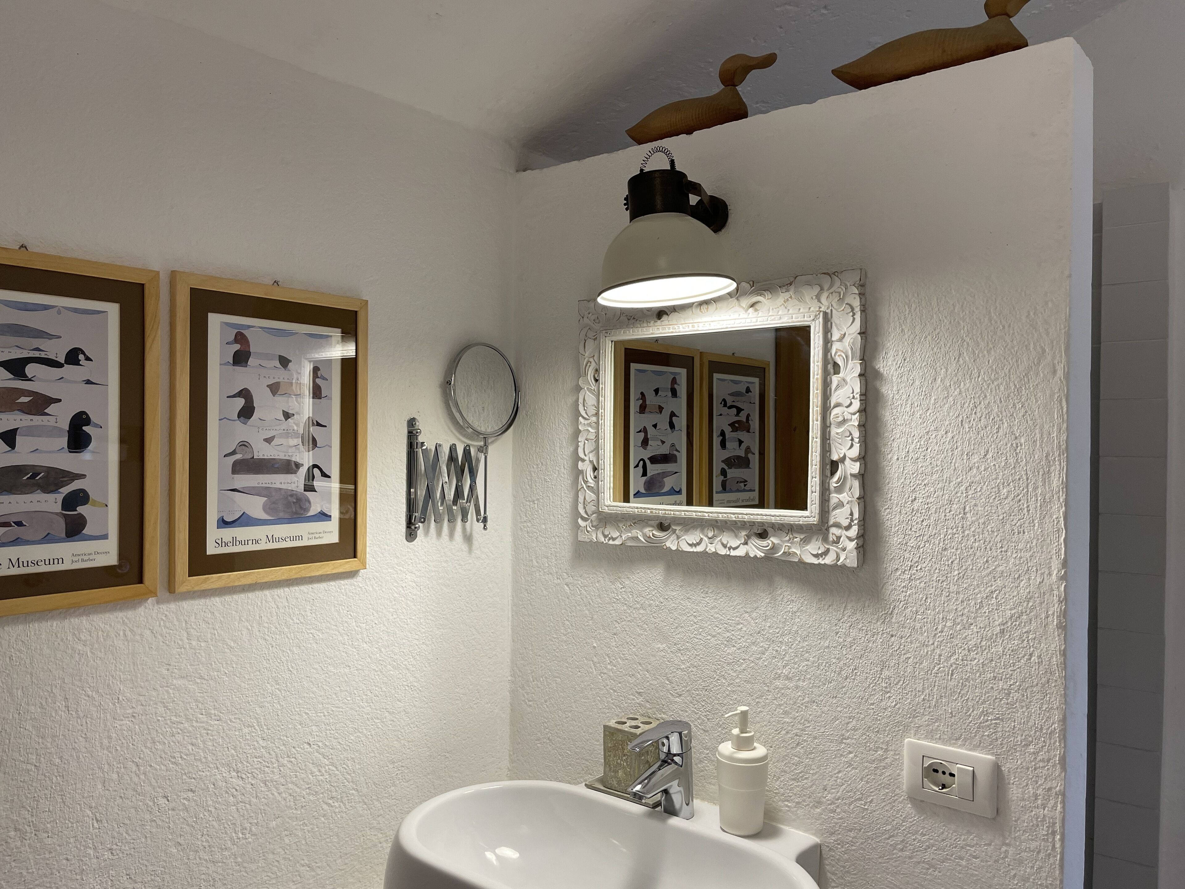 Un baño con un lavamanos blanco, un espejo y dos cuadros en la pared.