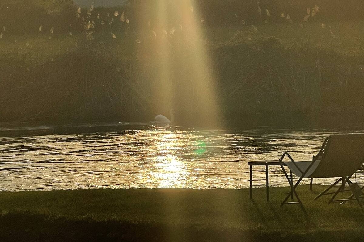 Un coucher de soleil sur une étendue d’eau, avec une chaise et une table sur la rive.