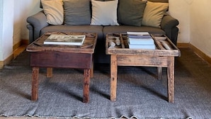 Ein gemütliches Wohnzimmer mit einer Couch, zwei Holztischen und einem Bücherregal mit verschiedenen Gegenständen.