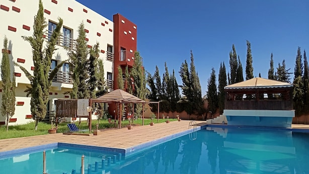 Una piscina con cubierta de madera, un pabellón y un edificio con paredes de color rojo y blanco.