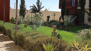 Un patio con diversas plantas, un camino empedrado y un edificio rojo con balcones.