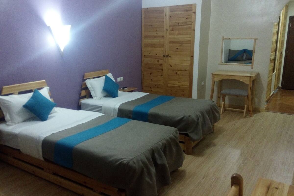 A room with two single beds, wooden headboards, a small wooden desk, a chair, and a wardrobe.