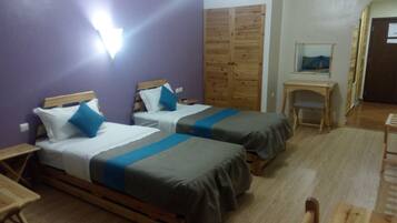 Una habitación con dos camas individuales, cabeceros de madera, un pequeño escritorio de madera, una silla y un armario.