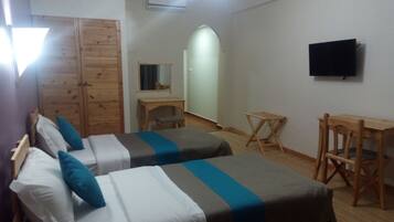 Una habitación con dos camas, un armario de madera, un escritorio, una silla y un televisor montado en la pared.