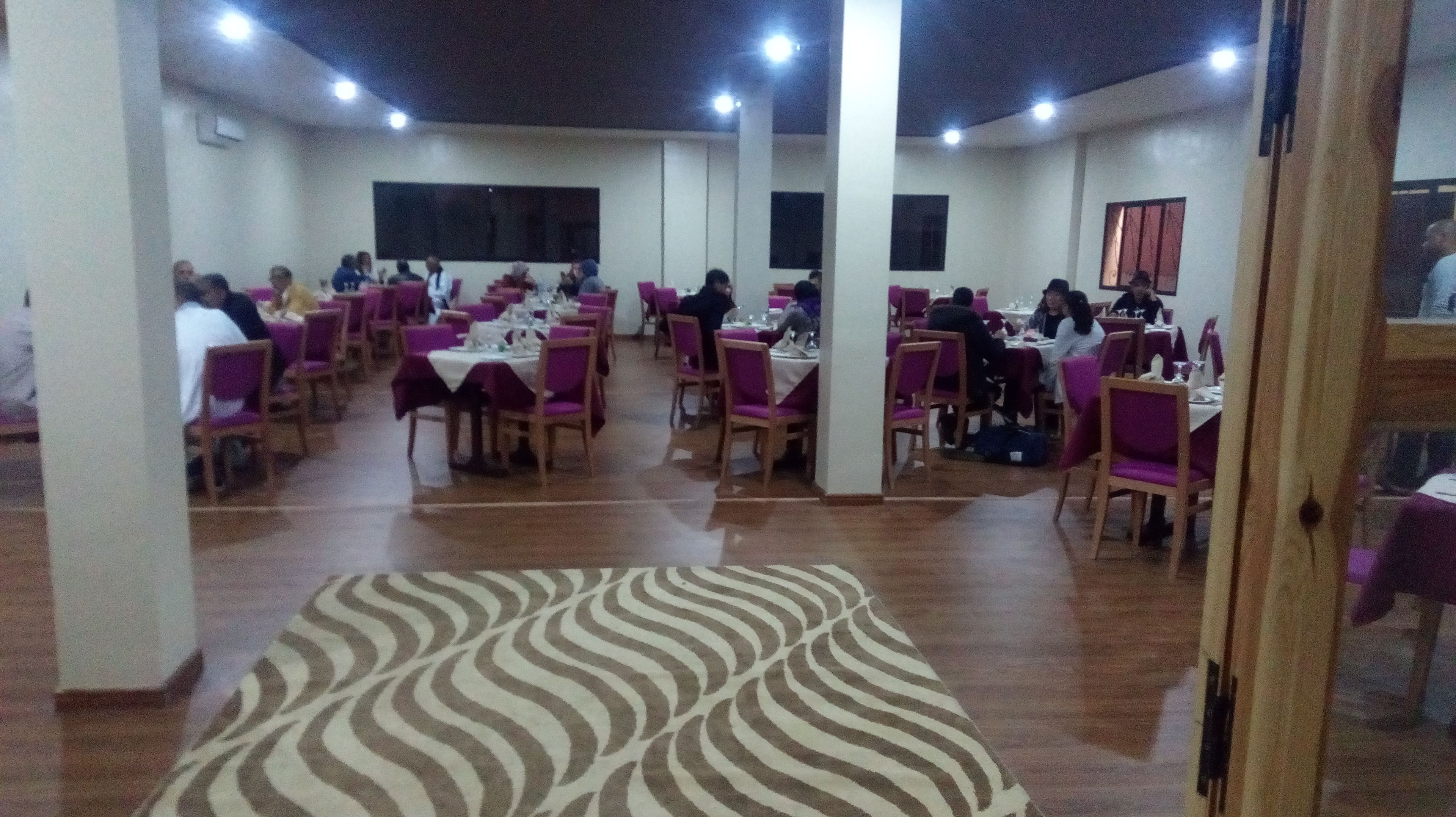 A dining area with multiple tables and chairs, arranged in a spacious layout with a patterned carpet.
