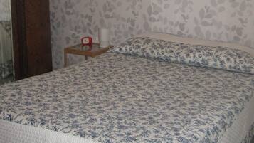 Ein Schlafzimmer mit einem Bett, einer Holztür, einem kleinen Tisch mit einer Uhr und floralem Wandpapier.