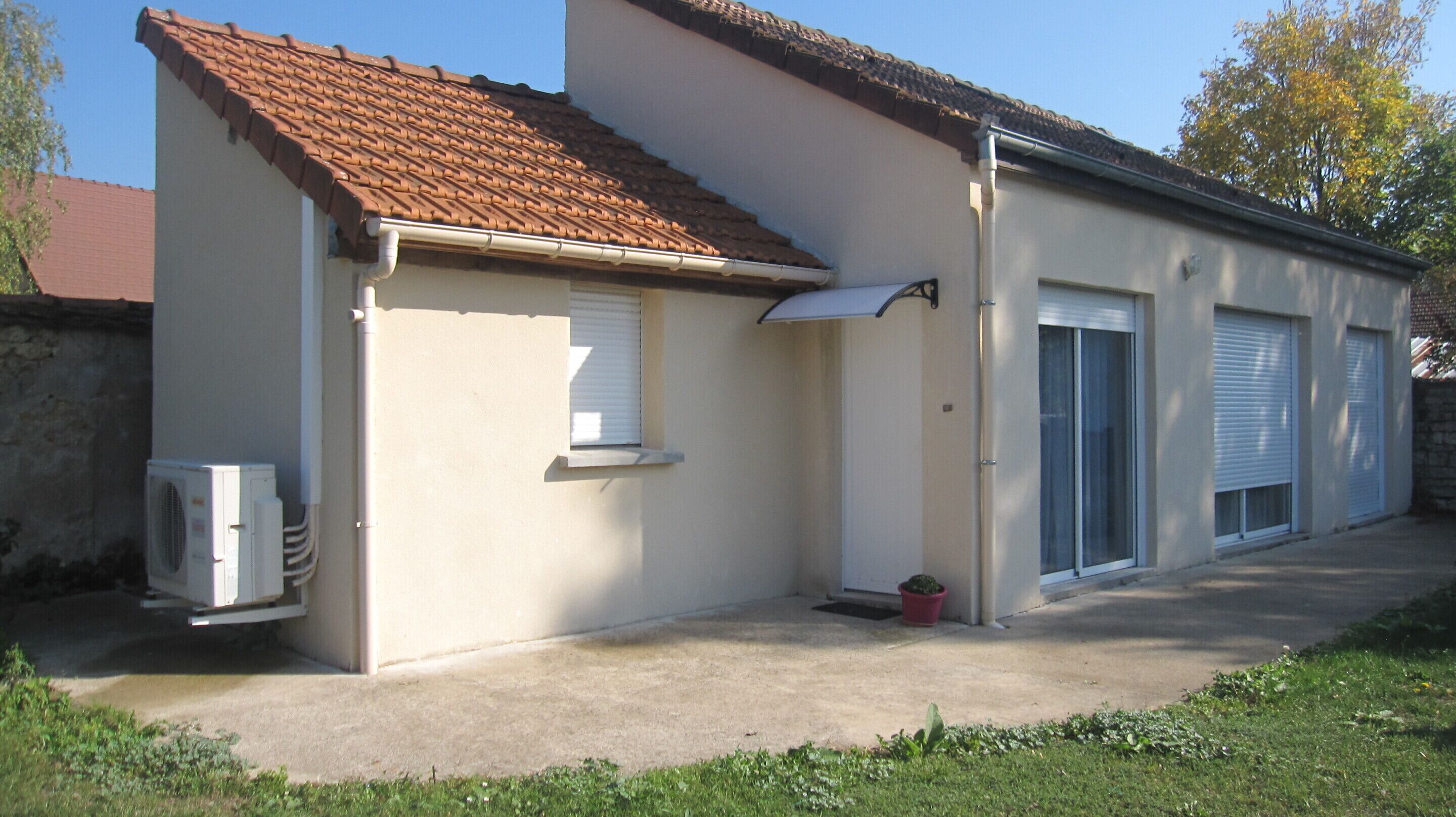 A single-story building with a tiled roof, a small window with shutters, and a door with a roller shutter.