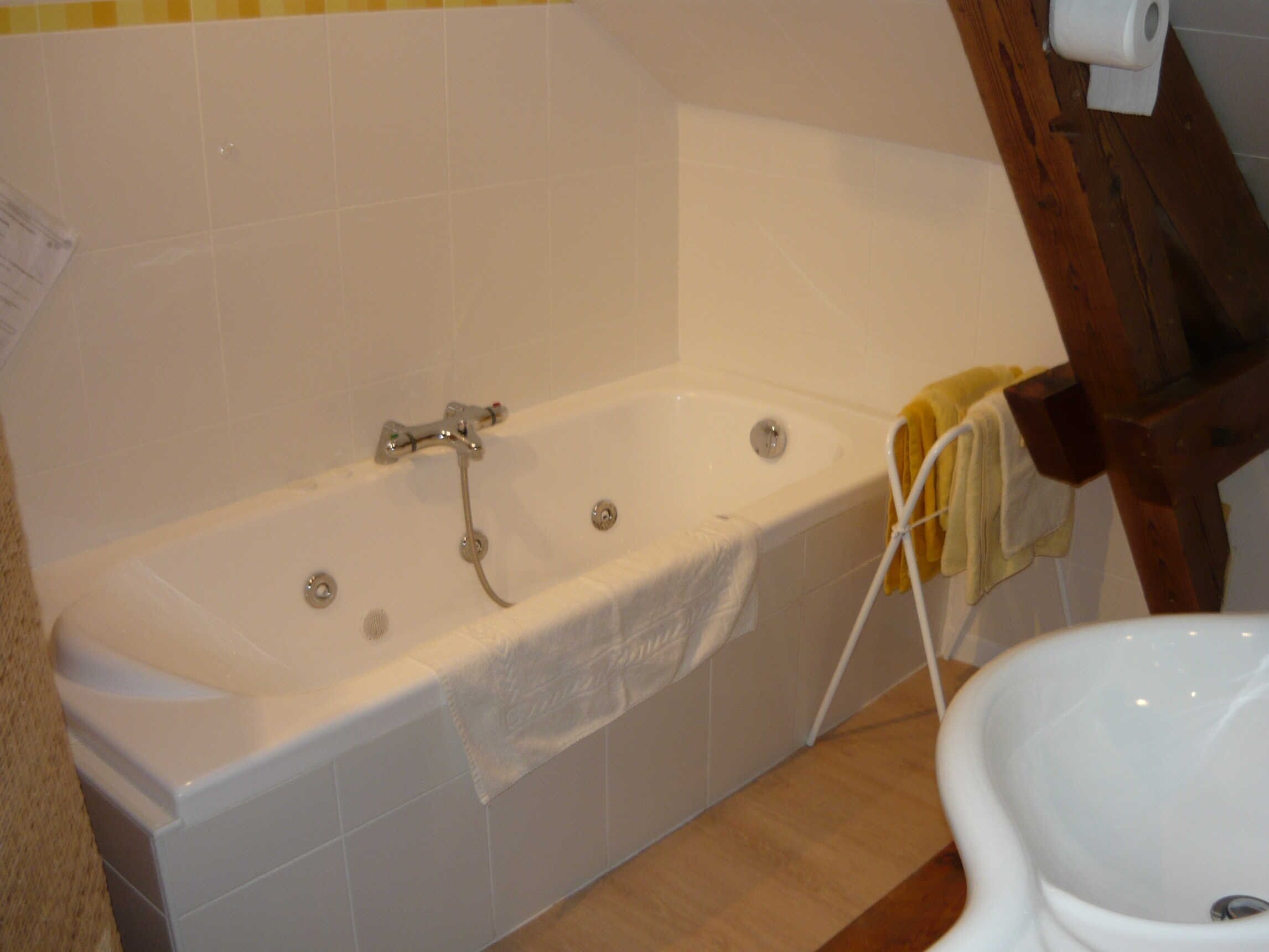 A bathroom with a bathtub, a toilet, and a wooden chair.