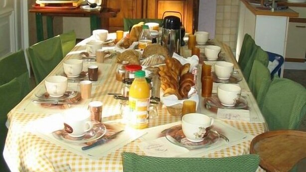 A dining table set with various dishes, cups, and a bottle, surrounded by chairs. - La Coutrotte Becquine (Heuilley-sur-Saone)