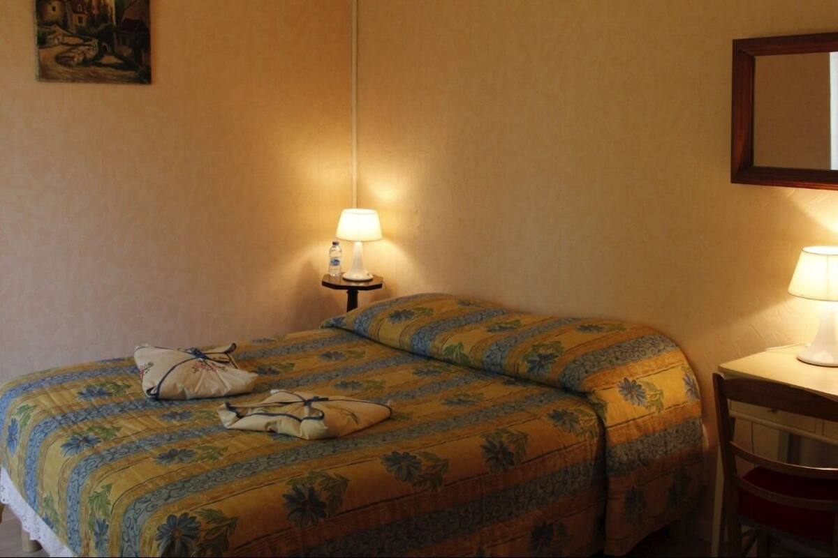 Une chambre d’hôtel avec un lit, une table de chevet avec une lampe, une chaise et un tableau au mur.