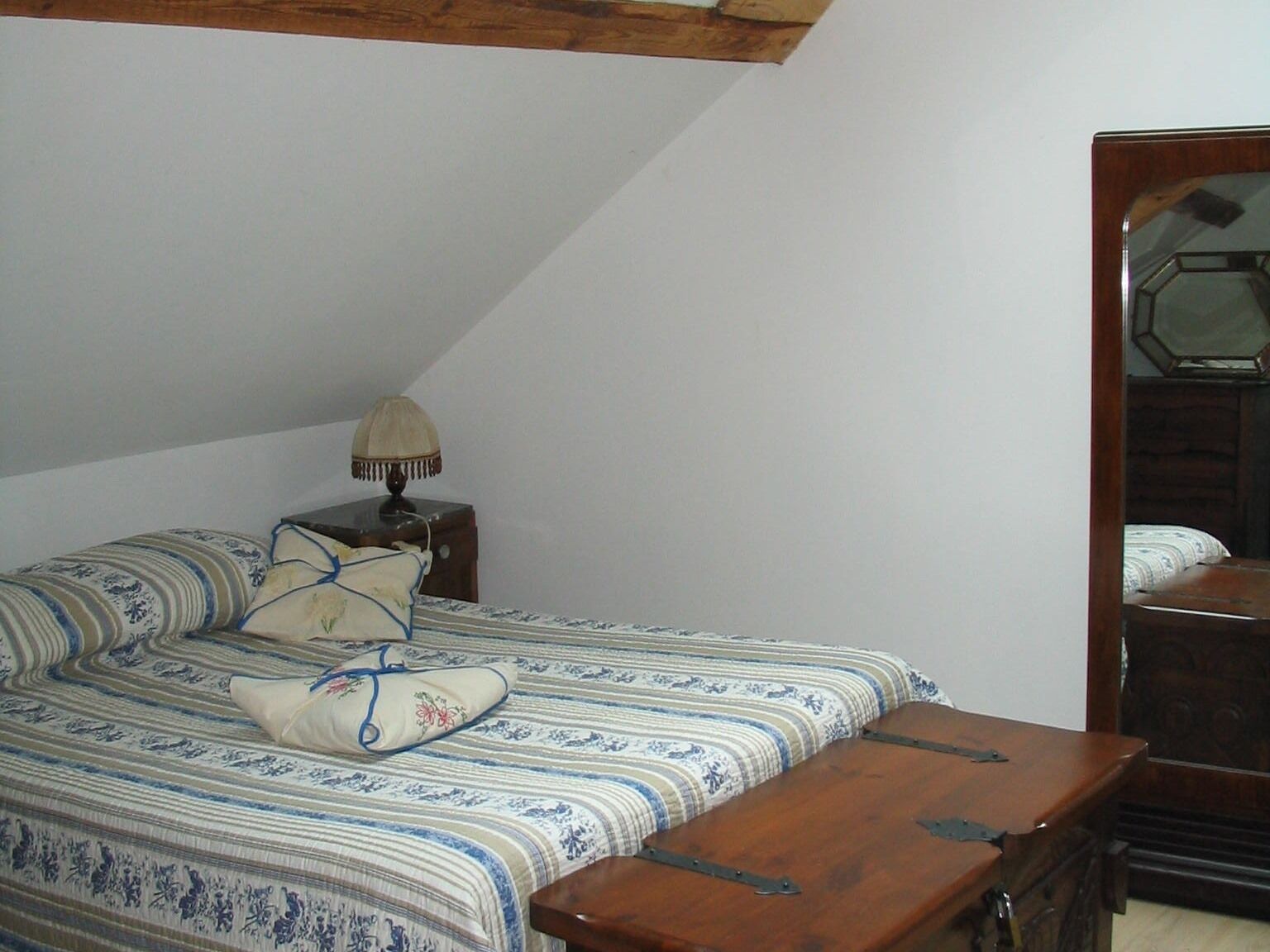 Een slaapkamer met een bed, nachtkastje, lamp, houten bankje en een dressoir.