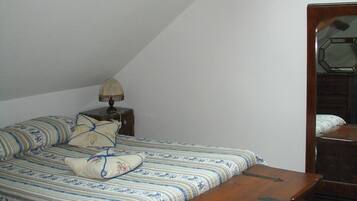Een slaapkamer met een bed, nachtkastje, lamp, houten bankje en een dressoir.