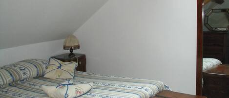 A bedroom with a bed, a nightstand, a lamp, a wooden bench, and a dresser.