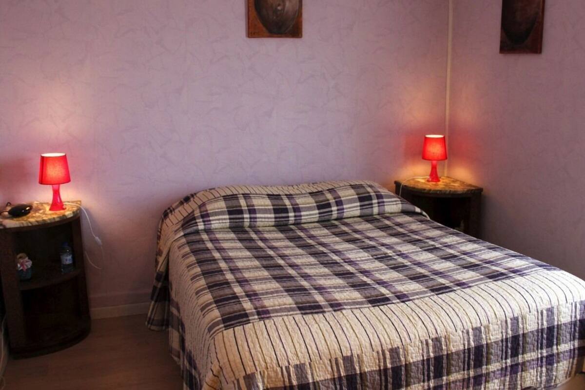 Une chambre à coucher avec une couvre-lit à carreaux, deux tables de chevet dotées de lampes rouges et deux tableaux accrochés au mur.