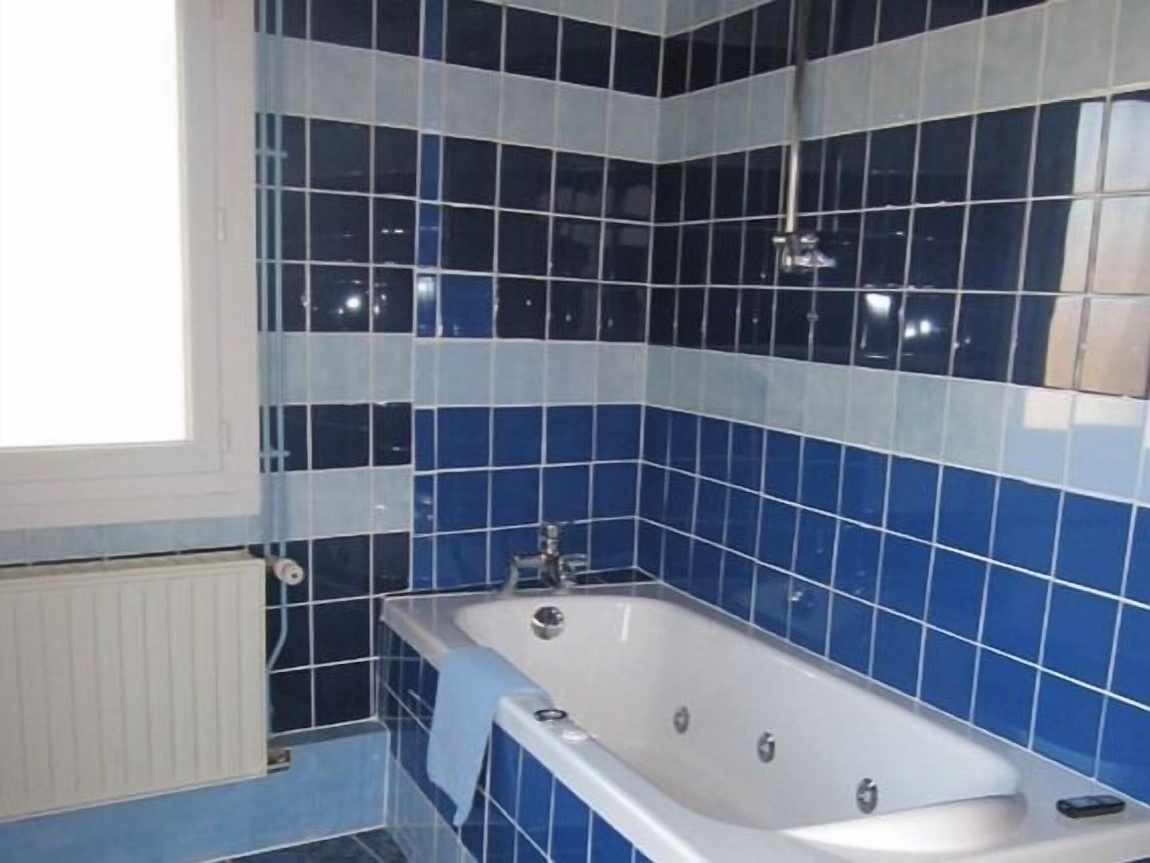 A bathroom with a bathtub, blue and white tiles, a window, and a radiator.