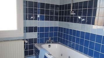 A bathroom with a bathtub, blue and white tiles, a window, and a radiator.