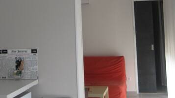 A room with a bed, a desk with a newspaper, and a chair.