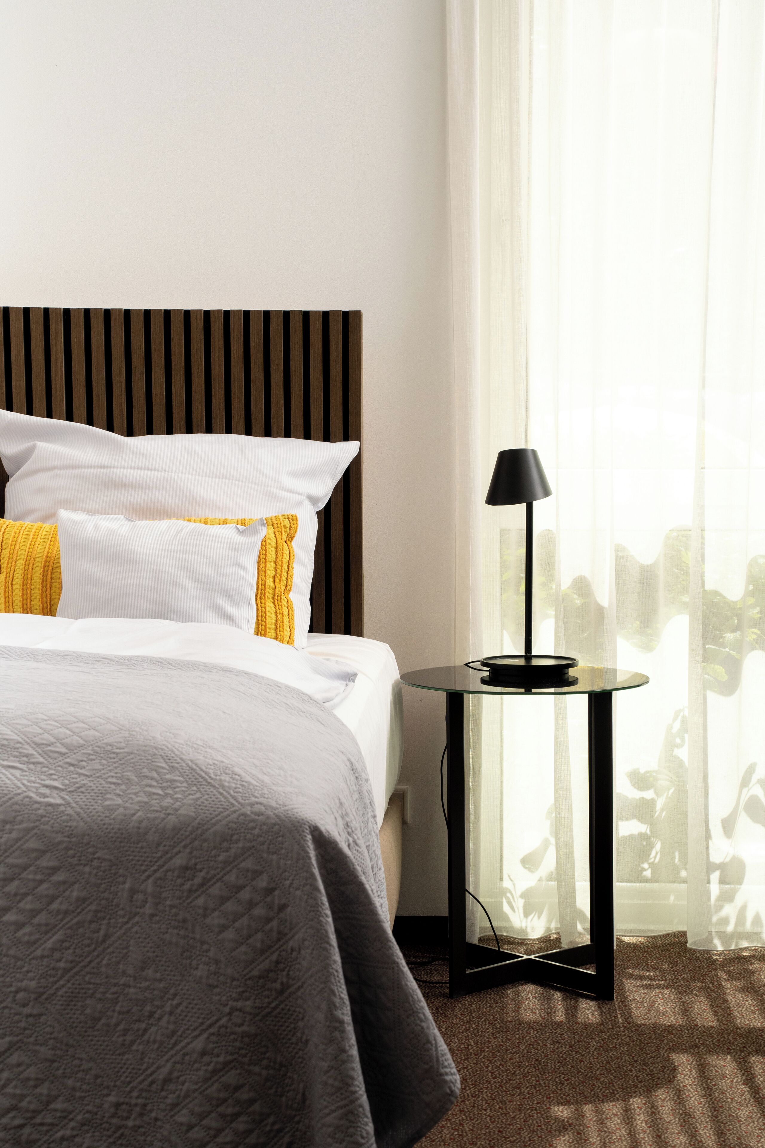 Una habitación de hotel con una cama, una mesita de noche con lámpara y cortinas traslúcidas.