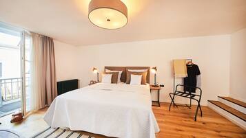 A hotel room with a bed, a chair, a radiator, and a window with curtains.