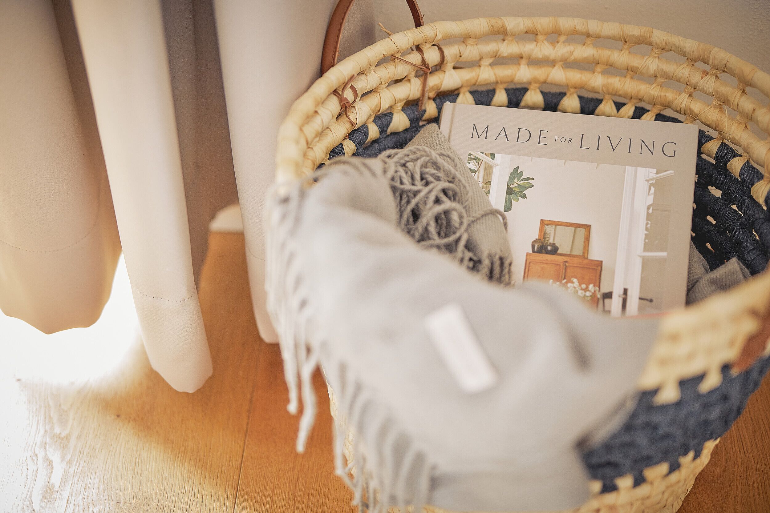 A wicker basket with a book titled "MADE for LIVING" and a grey fabric item.