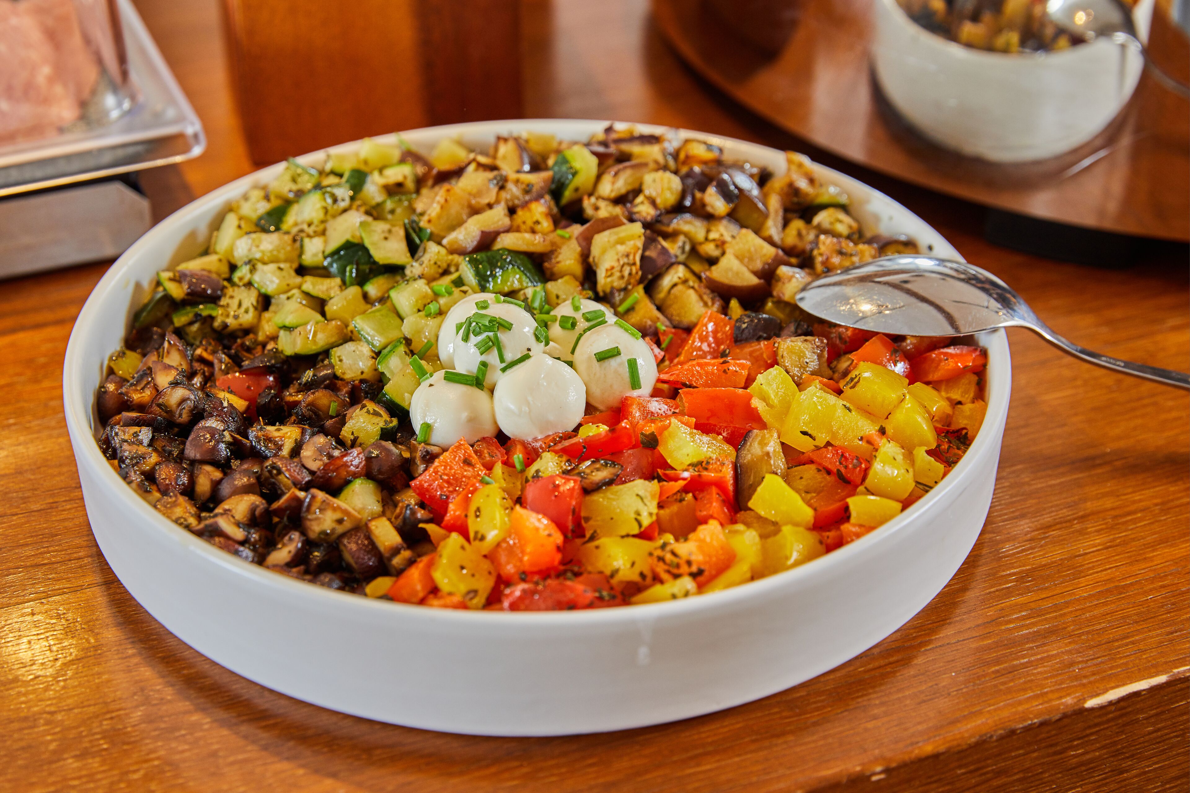 Un bol blanc rempli d’un plat de légumes colorés, garni de ciboulette, posé sur une table en bois.