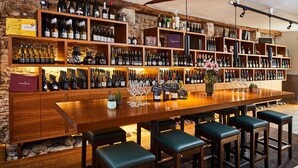 A bar with wooden shelves stocked with wine bottles, a long wooden bar, and several stools.