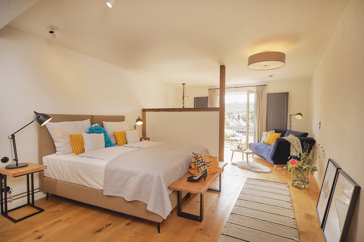 Een slaapkamer met een groot bed, nachtkastjes, een bankje, een klein tafeltje, een lamp, een sofa, een raam en uitzicht op het omliggende landschap.