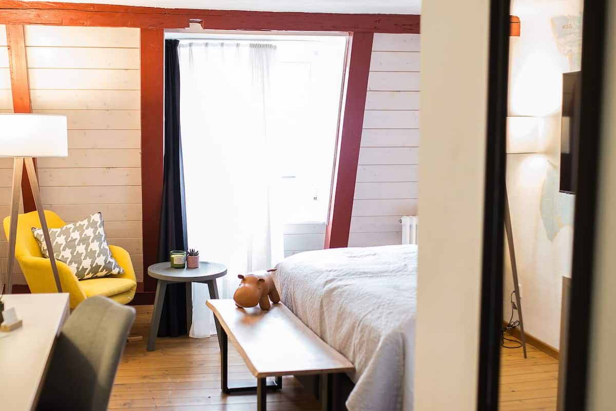 Hotelkamer met een bed, bureau, stoel, een klein tafeltje met lamp en een raam met gordijnen.