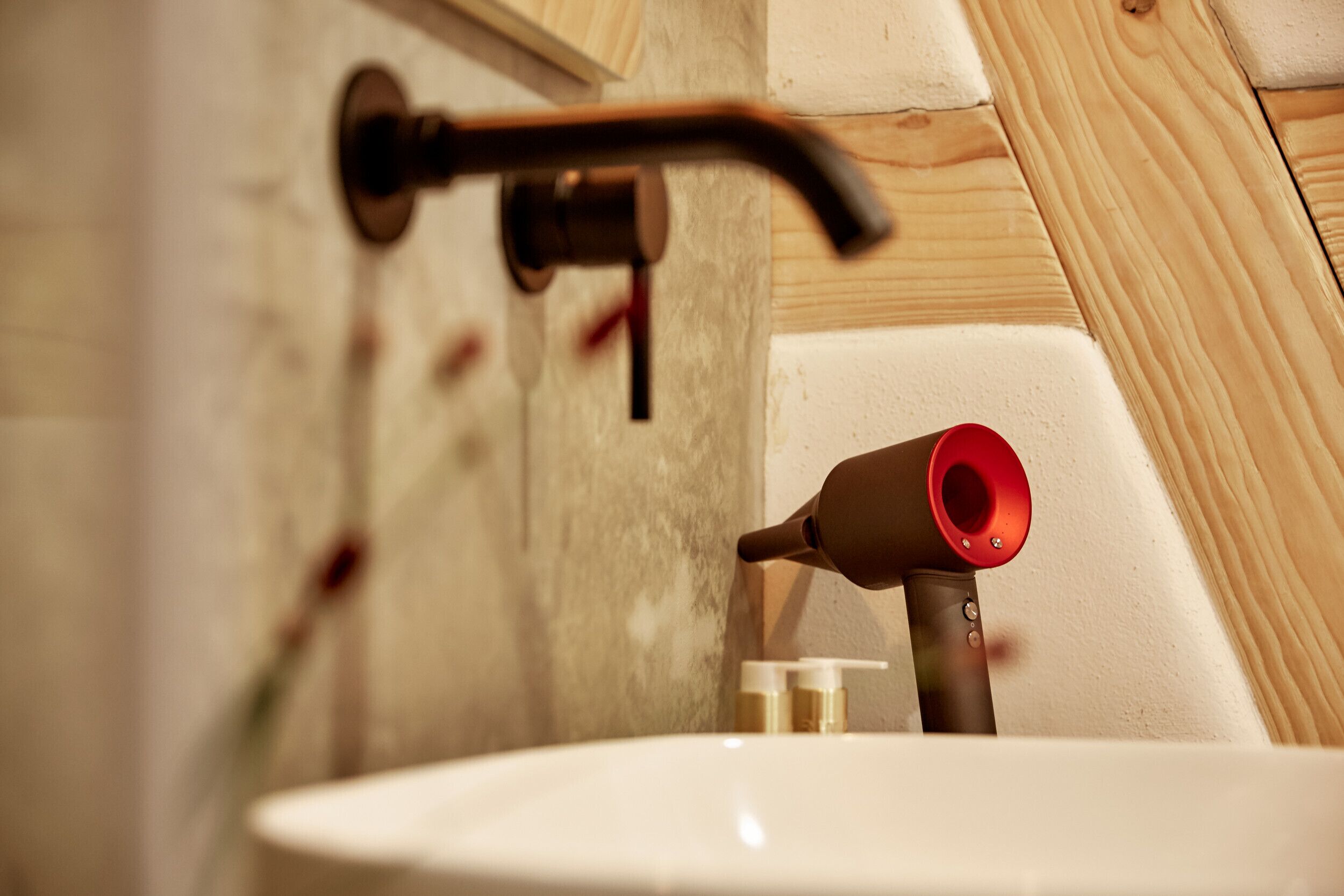 Une salle de bain avec un lavabo blanc, un robinet rouge et un mur recouvert de panneaux en bois.