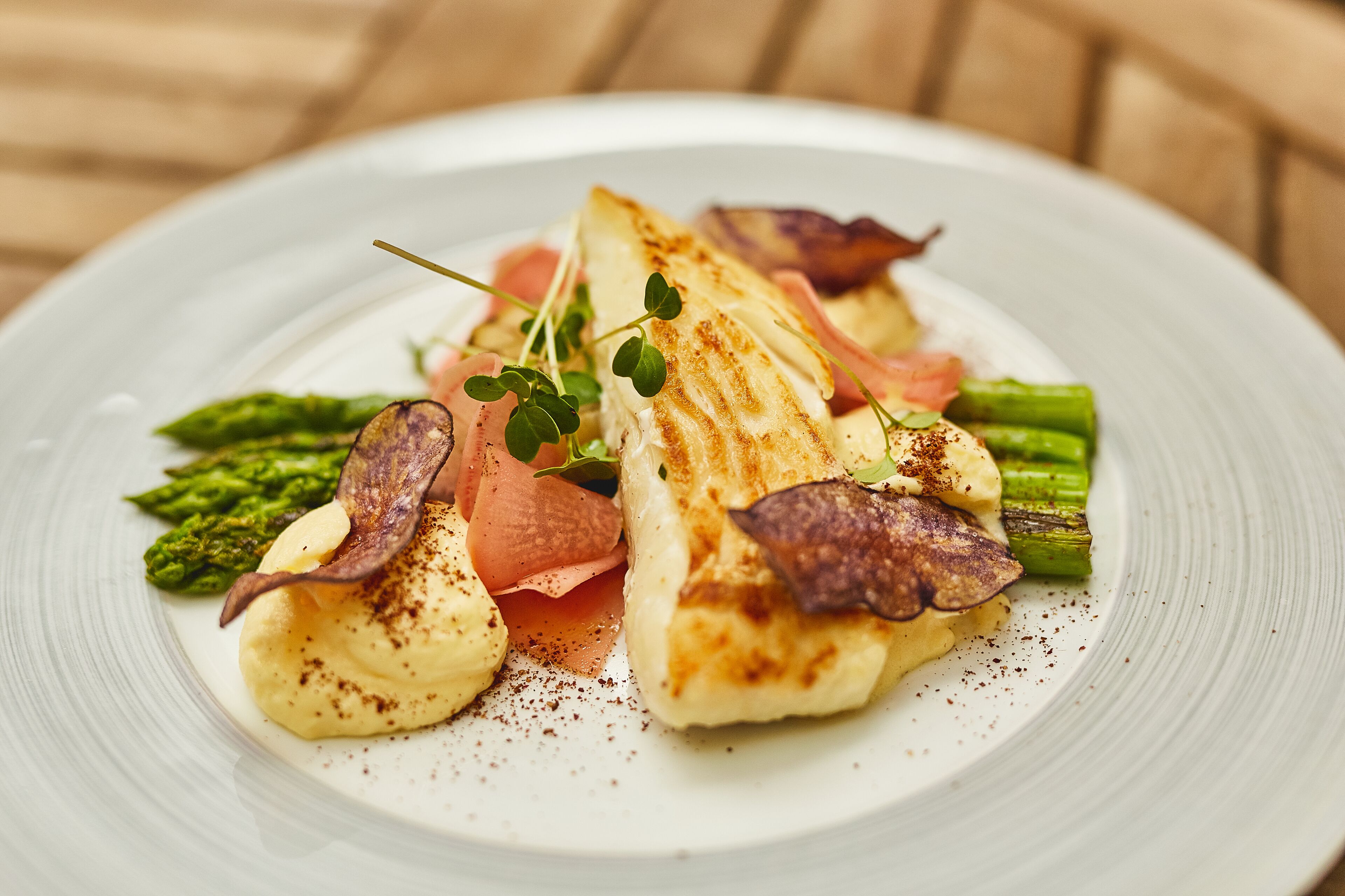 En tallerken med grillet fisk, asparges og en cremet sauce.